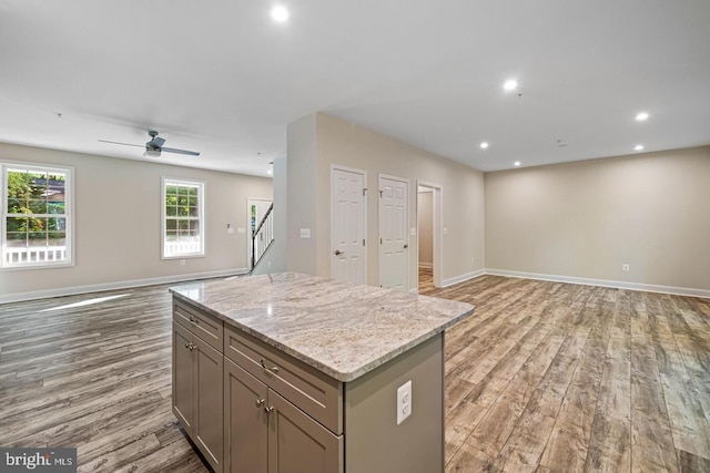 kitchen featuring light stone counters, a kitchen island, ceiling fan, and light wood-type flooring