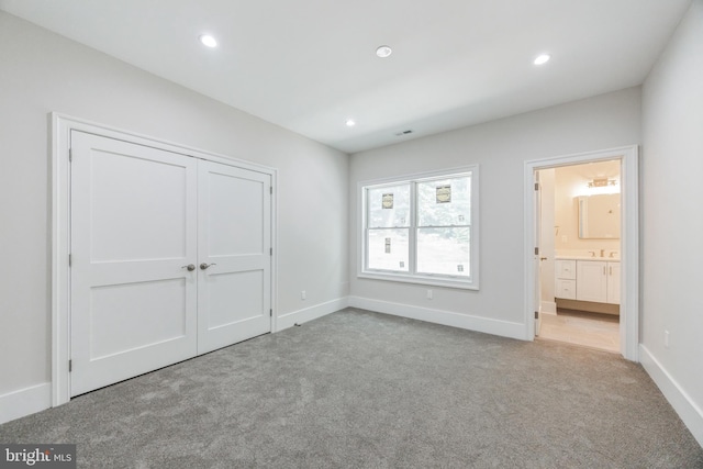 unfurnished bedroom featuring connected bathroom, a closet, light colored carpet, and sink