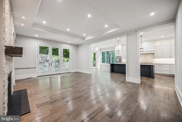 unfurnished living room featuring a raised ceiling, dark hardwood / wood-style flooring, a stone fireplace, and a wealth of natural light