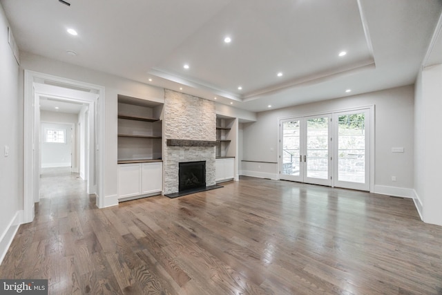 unfurnished living room with a raised ceiling, built in shelves, a stone fireplace, and hardwood / wood-style floors