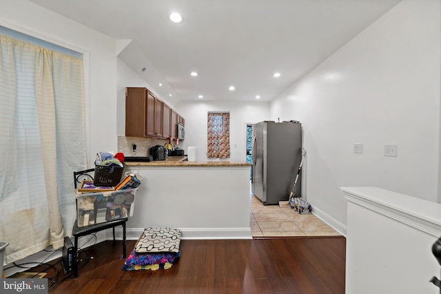 kitchen featuring backsplash, kitchen peninsula, appliances with stainless steel finishes, and light hardwood / wood-style flooring