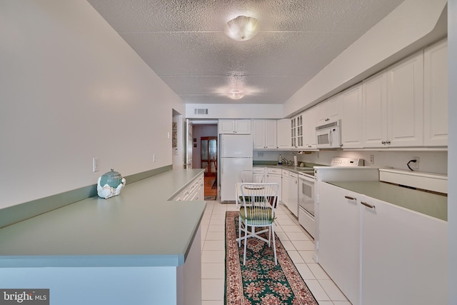 kitchen with a textured ceiling, white appliances, light tile patterned floors, and white cabinets