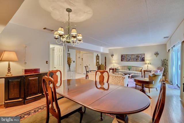 dining room featuring an inviting chandelier, a textured ceiling, and light wood-type flooring