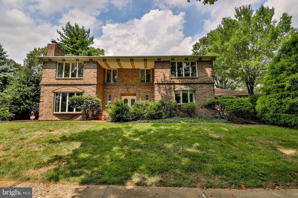 view of front of house with brick siding, a chimney, and a front lawn