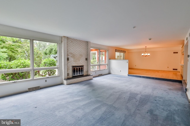 unfurnished living room featuring an inviting chandelier, a brick fireplace, and carpet floors