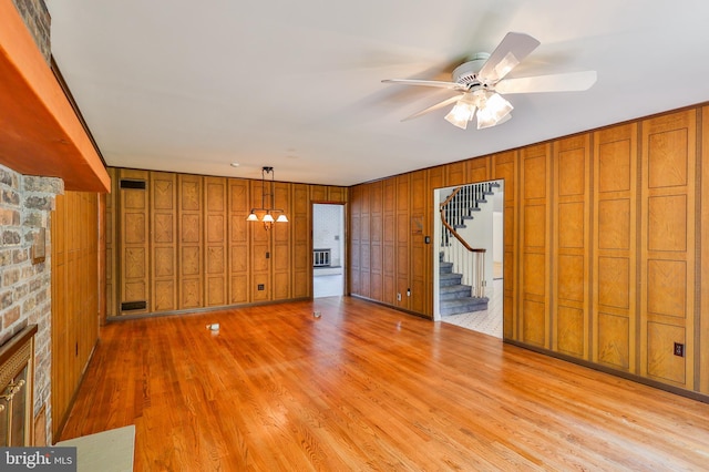 unfurnished living room with ceiling fan, wood walls, and light hardwood / wood-style floors