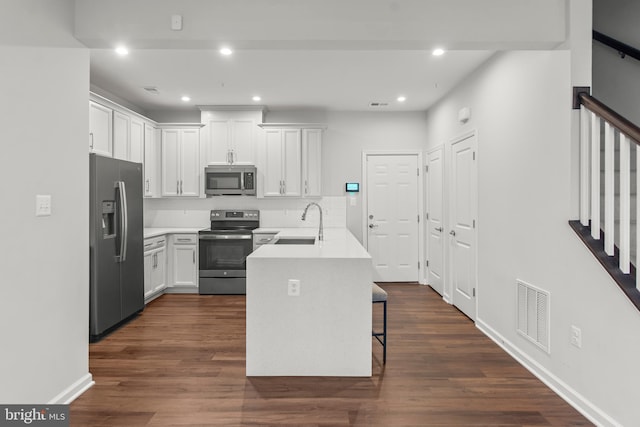 kitchen with white cabinets, appliances with stainless steel finishes, a breakfast bar, and dark hardwood / wood-style floors