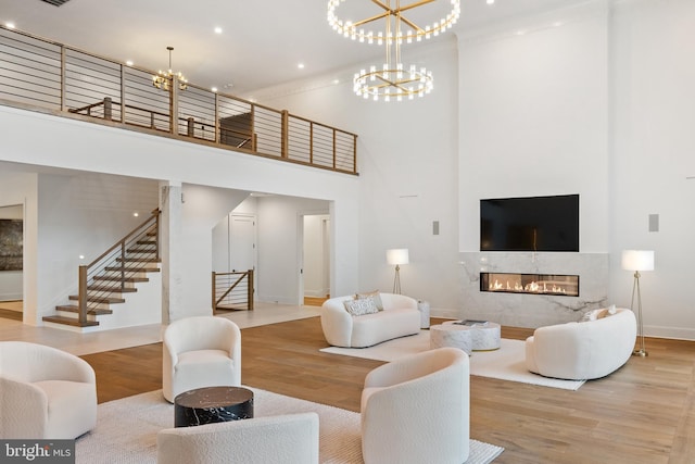 living room featuring light hardwood / wood-style floors, a chandelier, a towering ceiling, and a premium fireplace