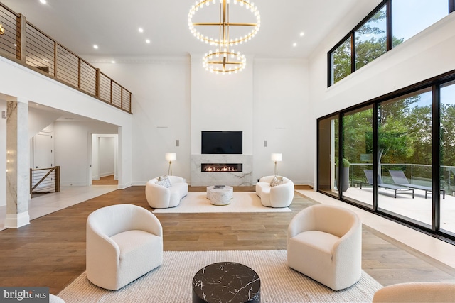 living room featuring wood-type flooring, a notable chandelier, crown molding, and a towering ceiling