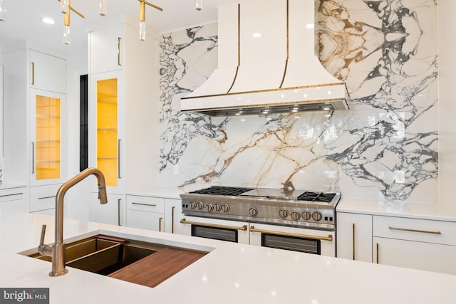 kitchen featuring white cabinetry, range with two ovens, premium range hood, backsplash, and sink