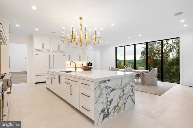 kitchen featuring built in refrigerator, pendant lighting, white cabinetry, sink, and a kitchen island with sink