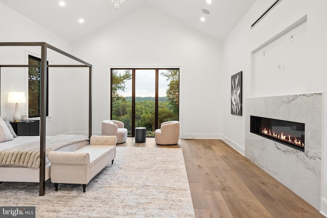 bedroom with high vaulted ceiling, a premium fireplace, and hardwood / wood-style flooring