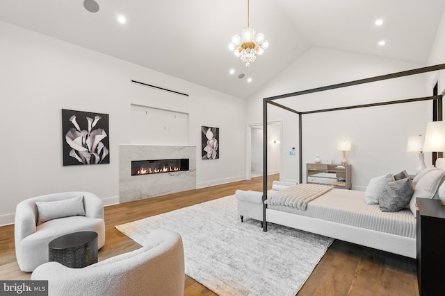 bedroom with high vaulted ceiling, wood-type flooring, a notable chandelier, and a premium fireplace