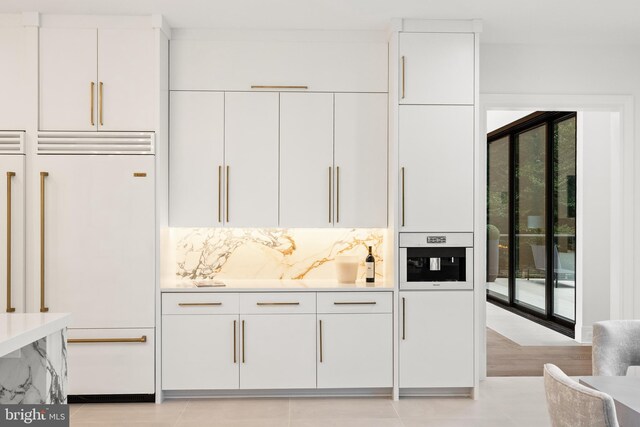 bar featuring white cabinetry, backsplash, paneled refrigerator, and light tile patterned floors