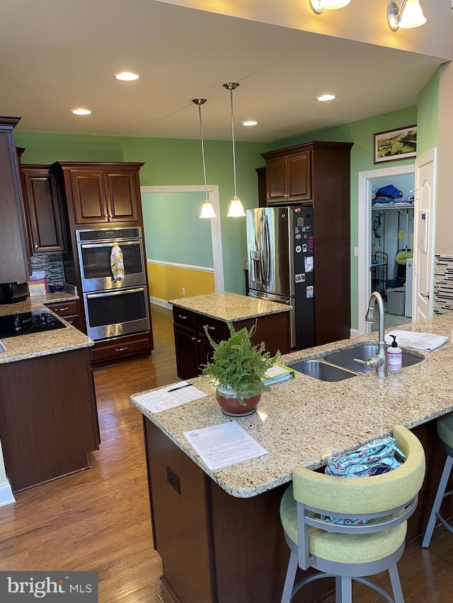 kitchen with sink, light stone counters, decorative light fixtures, a center island with sink, and appliances with stainless steel finishes