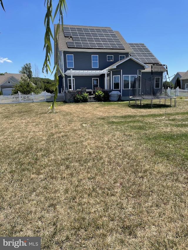 rear view of house featuring a lawn, a trampoline, and solar panels