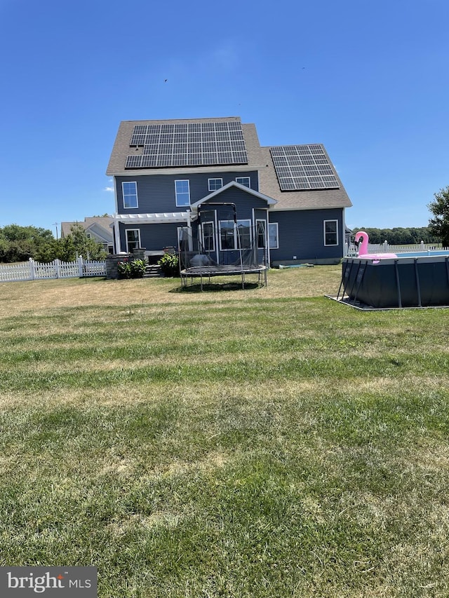 rear view of house with a fenced in pool, a yard, solar panels, and a trampoline