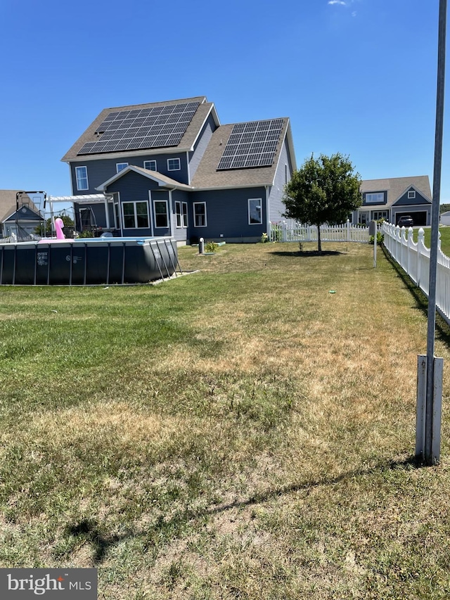 rear view of property with solar panels, a fenced in pool, and a lawn