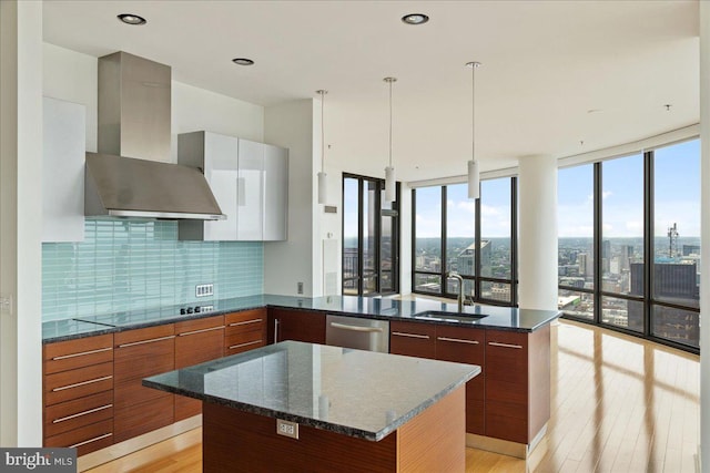 kitchen with dishwasher, pendant lighting, dark stone counters, and wall chimney range hood