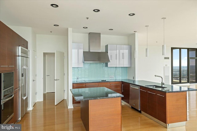 kitchen with sink, an island with sink, stainless steel appliances, and wall chimney range hood