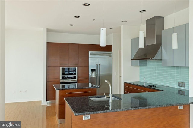 kitchen featuring pendant lighting, backsplash, wall chimney range hood, sink, and built in refrigerator