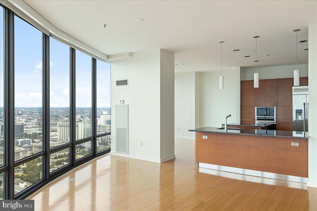 kitchen with dark stone counters, hanging light fixtures, built in appliances, light wood-type flooring, and a wall of windows