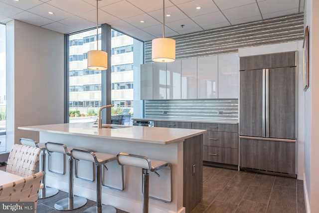 kitchen featuring a kitchen island with sink, sink, paneled fridge, and decorative light fixtures