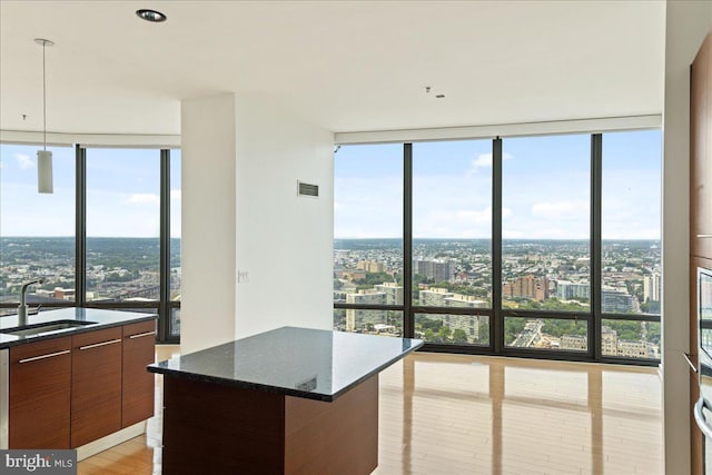 kitchen featuring floor to ceiling windows, sink, decorative light fixtures, dark stone countertops, and a kitchen island