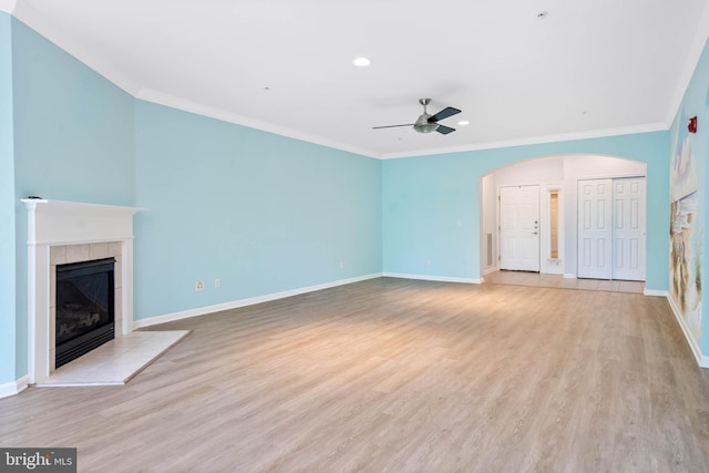 unfurnished living room featuring a tiled fireplace, ornamental molding, ceiling fan, and light hardwood / wood-style floors