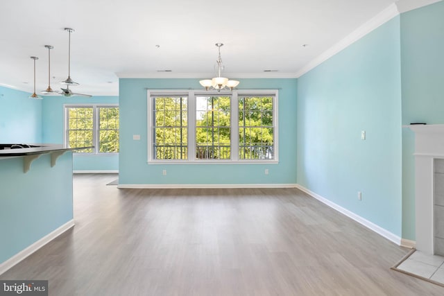 unfurnished living room featuring a healthy amount of sunlight, ornamental molding, ceiling fan with notable chandelier, and hardwood / wood-style floors