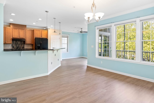 kitchen featuring tasteful backsplash, light wood-type flooring, black fridge, decorative light fixtures, and ornamental molding