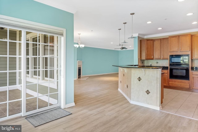 kitchen with tasteful backsplash, light wood-type flooring, ceiling fan with notable chandelier, black appliances, and pendant lighting