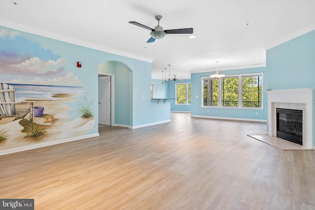 unfurnished living room with a tiled fireplace, ceiling fan with notable chandelier, and light hardwood / wood-style floors