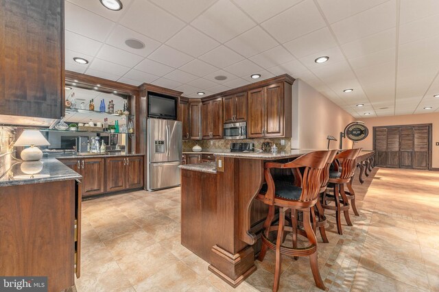 kitchen featuring dark stone countertops, kitchen peninsula, appliances with stainless steel finishes, and tasteful backsplash