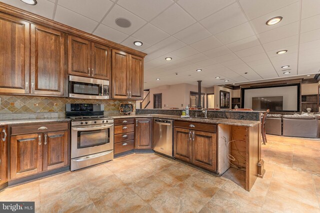 kitchen with kitchen peninsula, decorative backsplash, sink, and appliances with stainless steel finishes