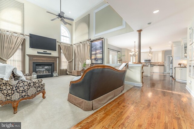 living room with ceiling fan with notable chandelier, a high ceiling, light wood-type flooring, and crown molding