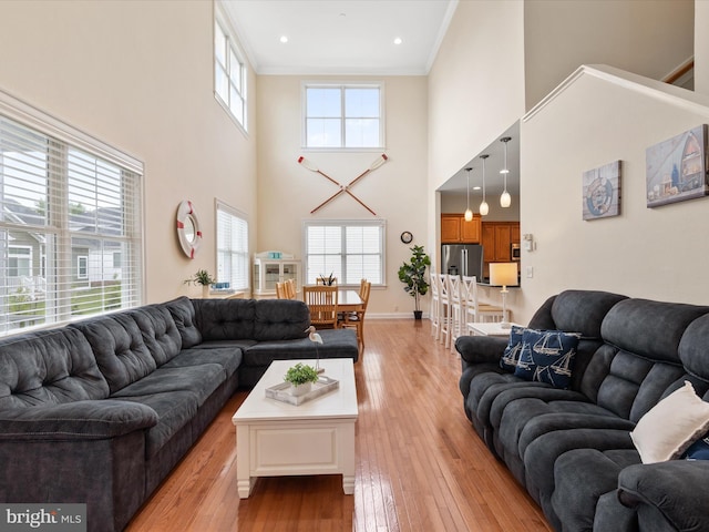 living room with a towering ceiling, light hardwood / wood-style floors, and ornamental molding