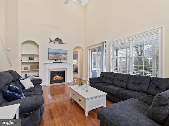 living room featuring ceiling fan, built in features, a towering ceiling, and light hardwood / wood-style floors