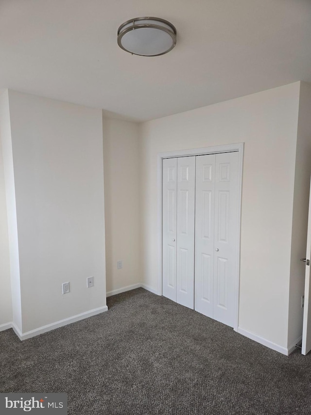 unfurnished bedroom with dark colored carpet and a closet