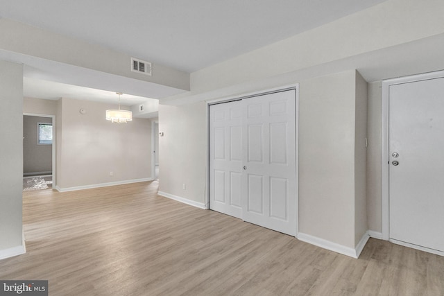 unfurnished bedroom featuring a closet, an inviting chandelier, and light wood-type flooring