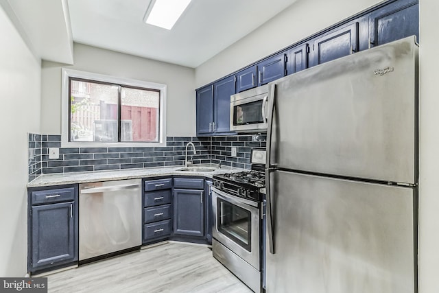 kitchen with light hardwood / wood-style floors, appliances with stainless steel finishes, blue cabinetry, tasteful backsplash, and sink