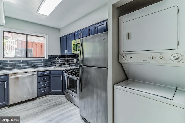 kitchen featuring appliances with stainless steel finishes, blue cabinetry, backsplash, stacked washer / dryer, and sink