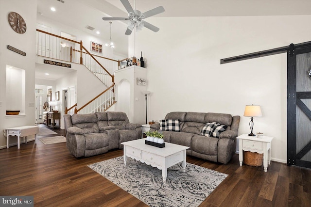 living room with ceiling fan, a towering ceiling, dark hardwood / wood-style floors, and a barn door