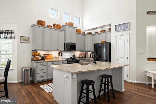 kitchen featuring an island with sink, a breakfast bar area, stainless steel appliances, light stone counters, and sink