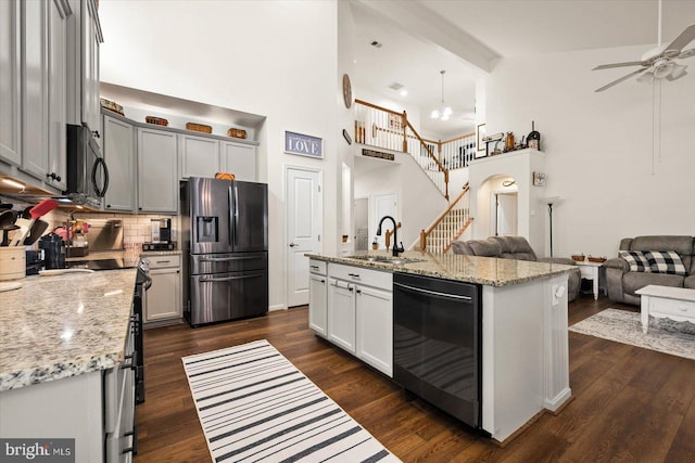 kitchen featuring gray cabinetry, stainless steel appliances, sink, light stone counters, and a center island with sink