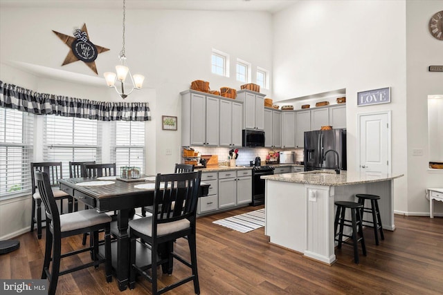 kitchen featuring electric stove, a kitchen island with sink, black fridge with ice dispenser, light stone counters, and a breakfast bar area