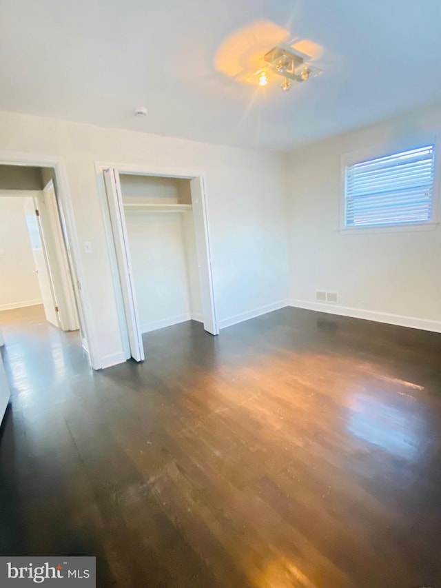 unfurnished bedroom featuring a closet, dark wood-style flooring, visible vents, and baseboards