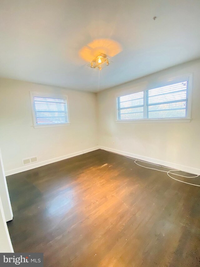 unfurnished room featuring dark wood-style floors, visible vents, and baseboards