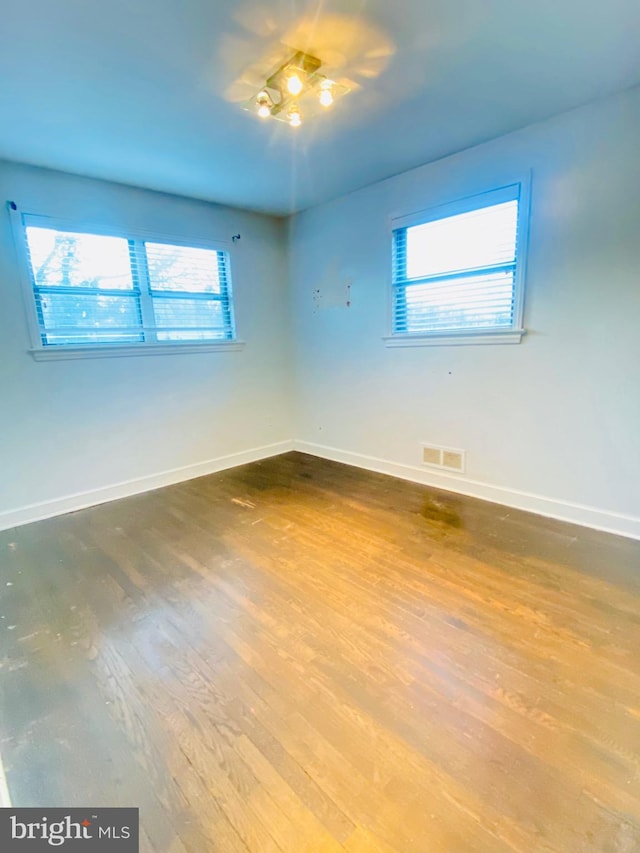 spare room featuring baseboards, visible vents, and wood finished floors