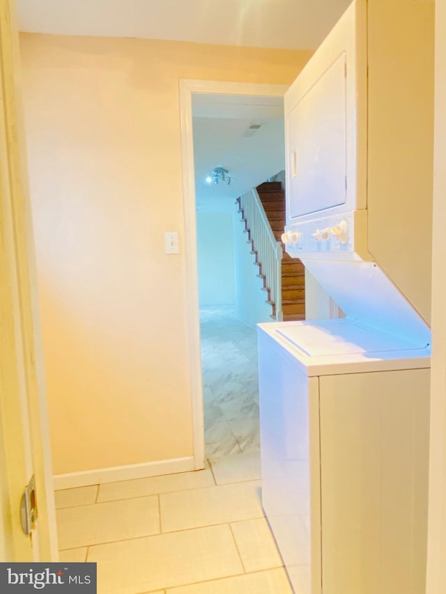 laundry room featuring stacked washer and dryer, laundry area, light tile patterned flooring, and baseboards